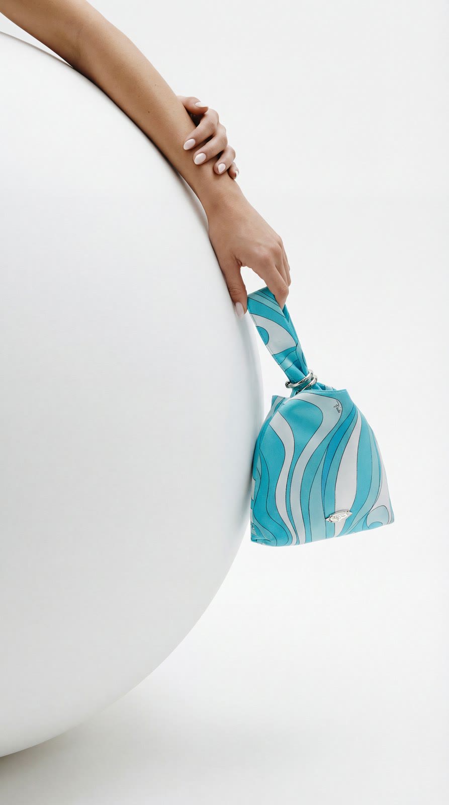 Brazo con bolso turquesa estampado sobre una esfera blanca.