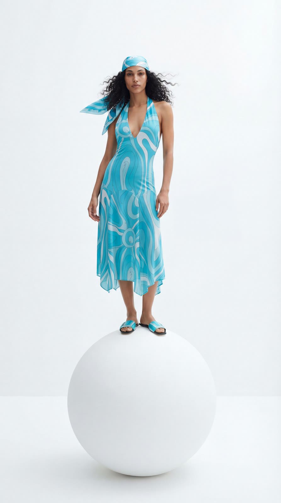 Figura con vestido turquesa estampado sobre una esfera blanca.
